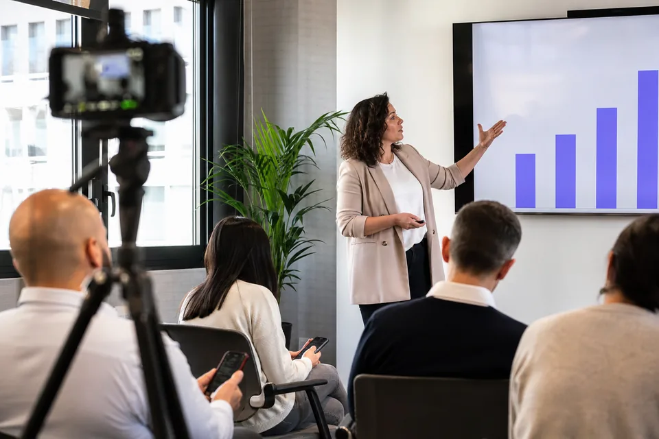 A trainer running a live session with phones out while a camera records it, the recording that later becomes a graded quiz